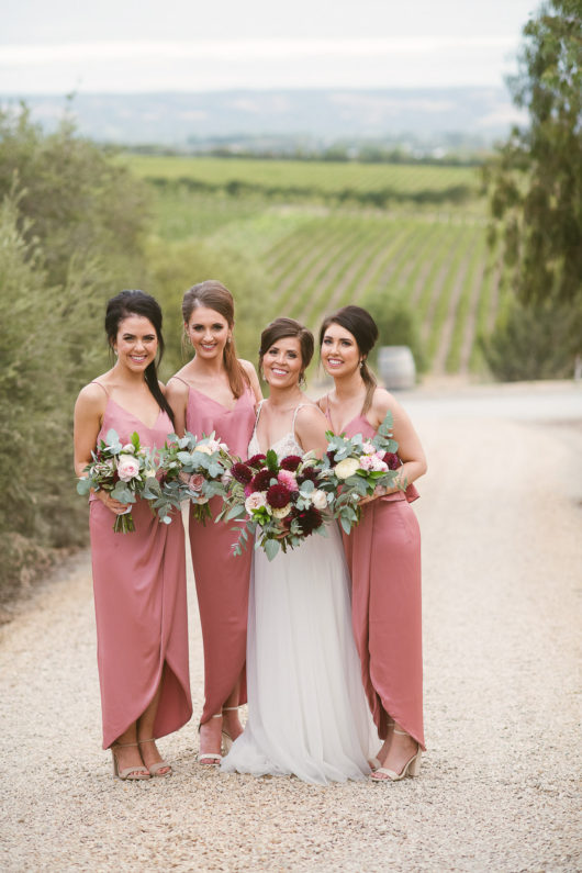 bride chelsea and three bridesmaids holding flowers by farmhouse flowers before wedding ceremony 