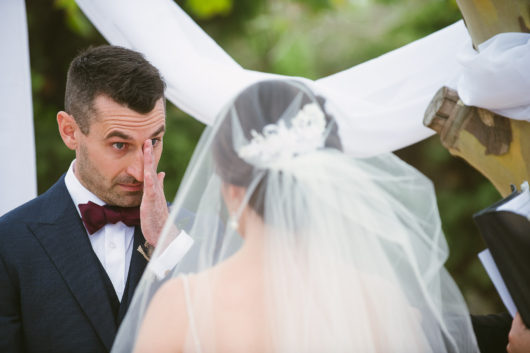 happy groom wiping a tear from his eye during winery wedding ceremony