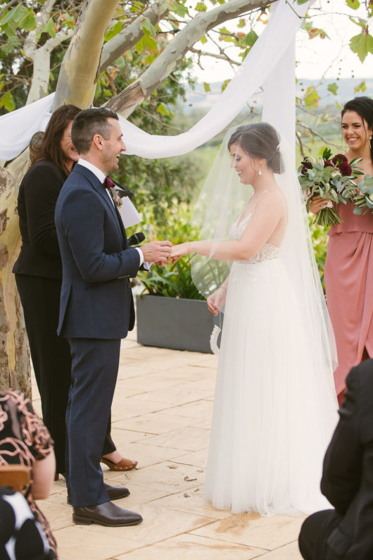 groom placing ring on brides finger in garden ceremony at beach road winery wedding