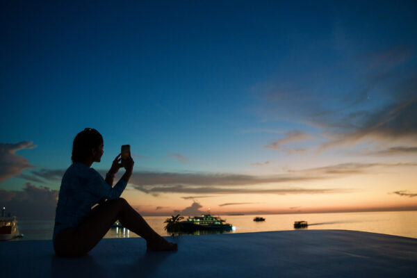 silhouette of conference attendee enjoying and photographing sunset with iphone on top deck of scubaspa