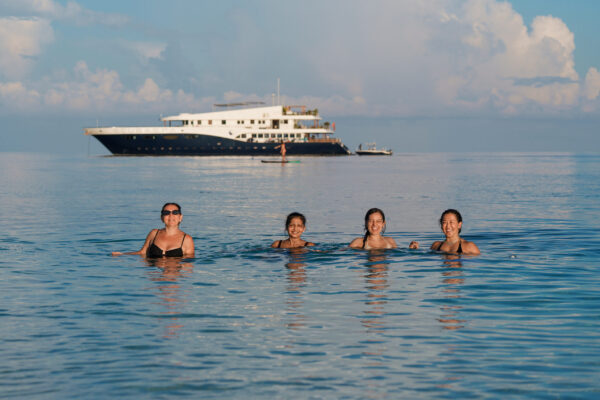 Conference attendees enjoy a cooling swim at sunset with scubapa anchored in the background on a calm evening on the Indian Ocean